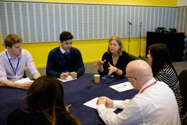 A group of people sitting around a table</p>
<p>Description automatically generated